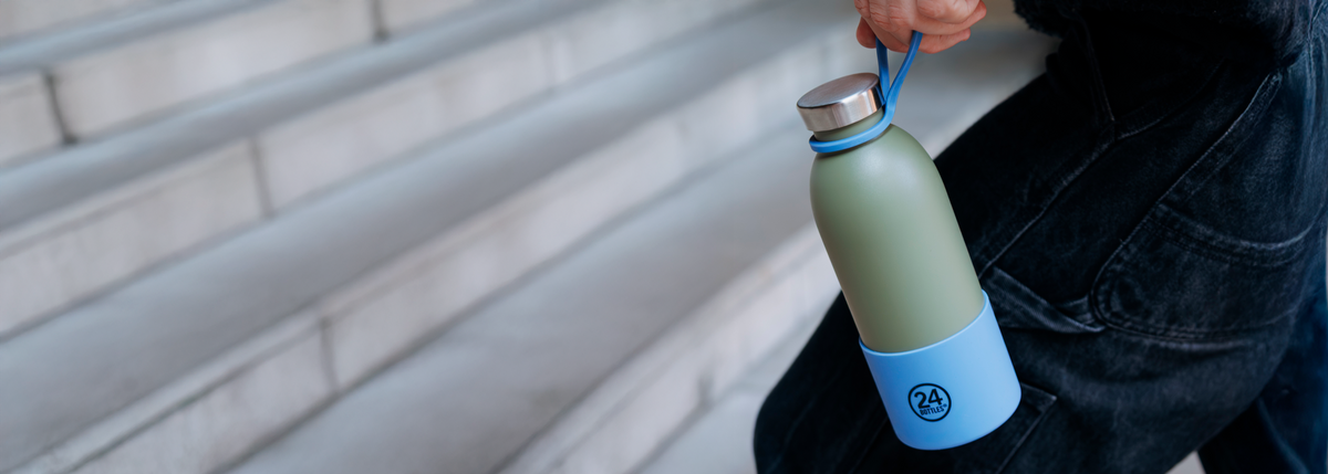 Person holding a green and blue water bottle with a blue strap against a blurred background