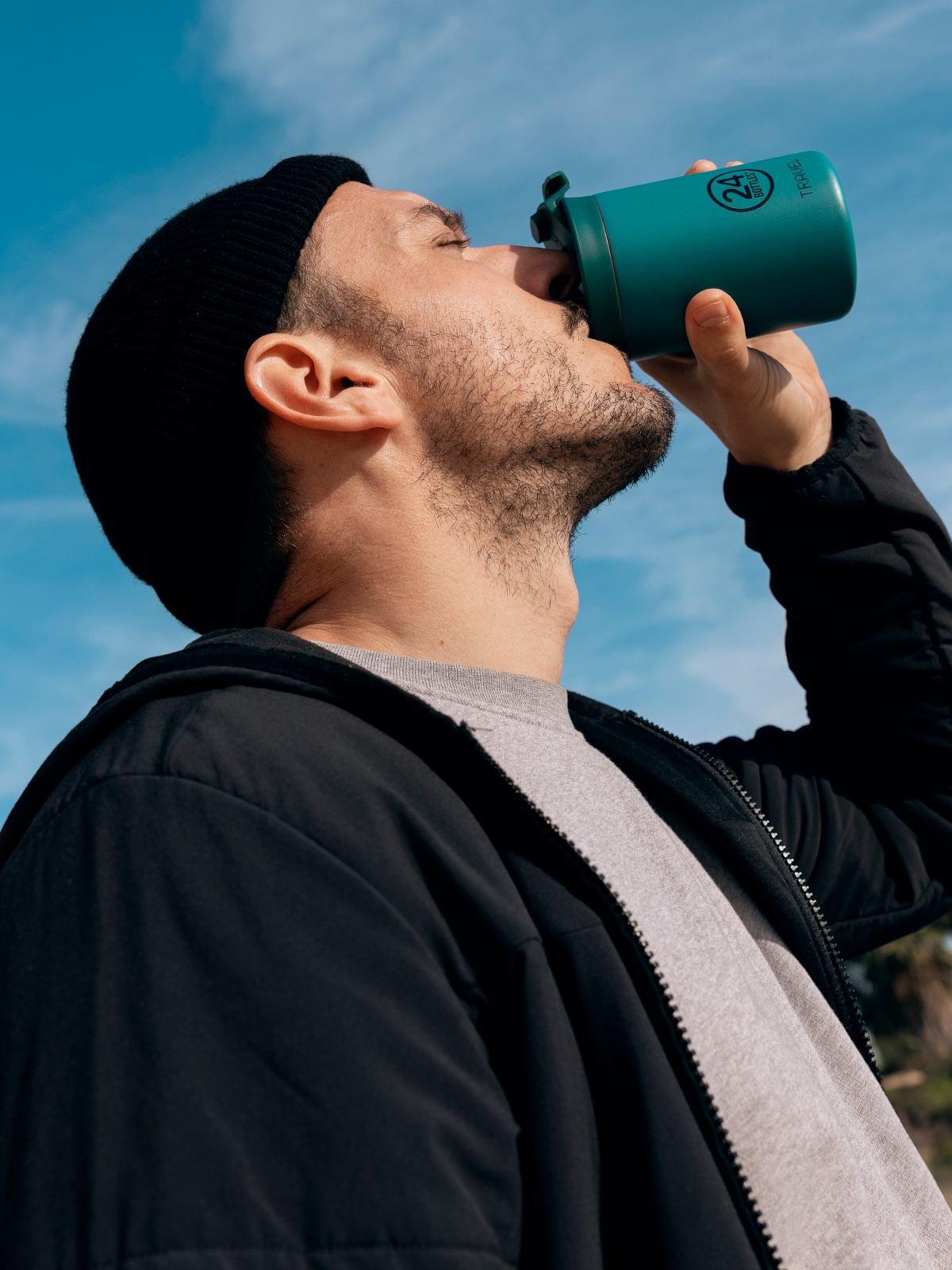 Man drinking from a teal insulated tumbler against a blue sky