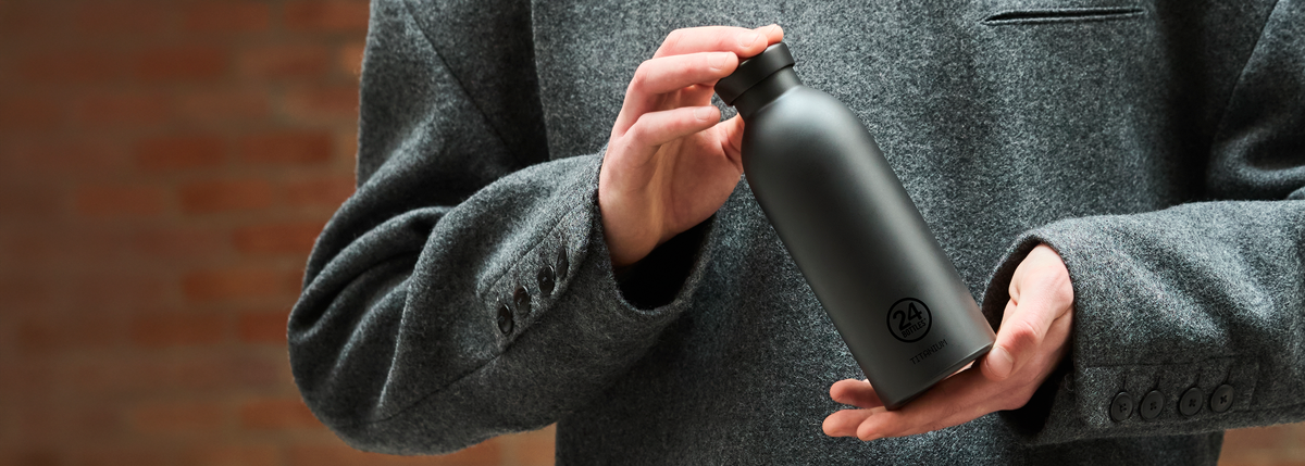 Person holding a black Titanium Bottle with 24Bottles logo, wearing a gray coat.