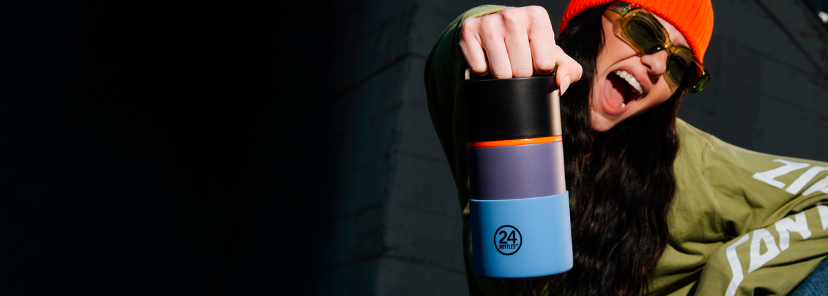 Person wearing an orange beanie and sunglasses holding a blue and black tumbler by its handle